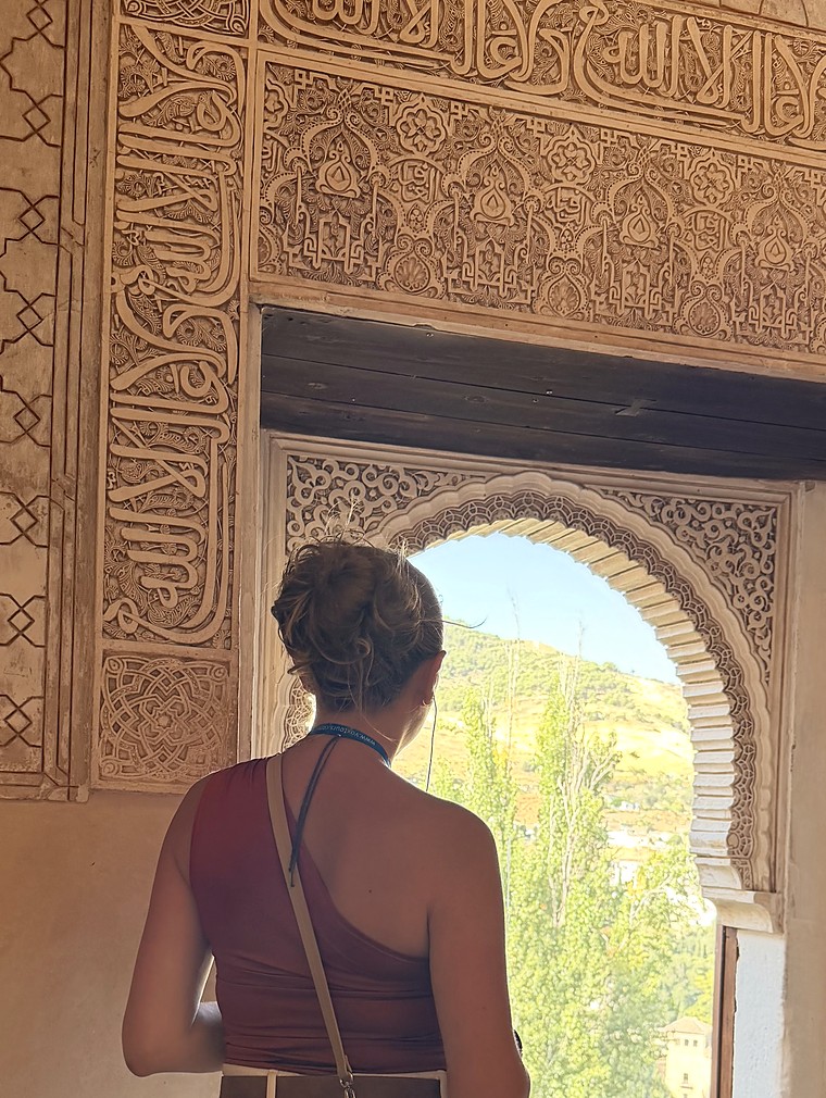 Hala Hijazi in the Alhambra, looking out through an arched window.